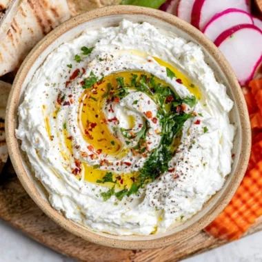 Creamy whipped feta dip served in a bowl, garnished with herbs and olive oil.