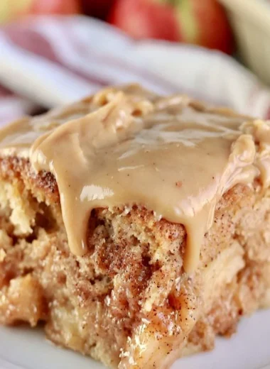 Slice of cozy Apple Dapple Cake topped with nuts and caramel drizzle.